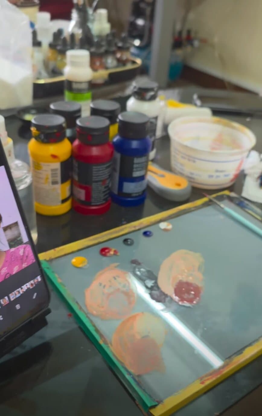 Studio paint bench with pots of acrylic paint, a mixing palette and a reference photo on a phone