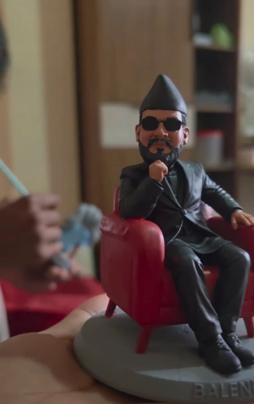 3D printed miniature of a bearded man in a black suit and dhaka topi seated in a red armchair